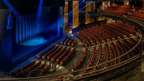 Teatersal med buede seterader, scene og balkong under blå belysning